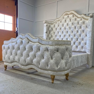 Puede incluir: Una cabecera capitoné blanca con un diseño curvo y detalles dorados. La cabecera está tapizada en un tejido suave y mullido.