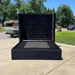 May include: A black upholstered bed frame with a tall headboard featuring a tufted design. The headboard is made of a soft, plush fabric.