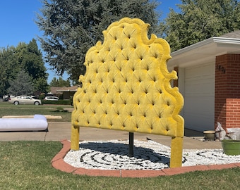 May include: A large, yellow, tufted headboard with a decorative, ornate design. The headboard is standing on a bed of white stones in a circular pattern.