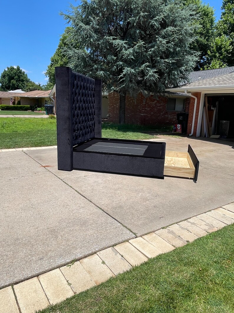 May include: Black upholstered bed frame with a tufted headboard and a pull-out storage drawer. The bed frame is on a concrete driveway.