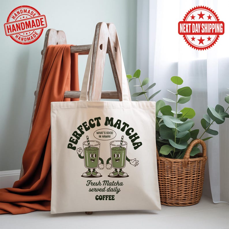 K&ouml;nnte beinhalten: Cremefarbene Tragetasche mit dem Schriftzug "PERFECT MATCHA" in Retro-Schrift und zwei Cartoon-Matcha-Getr&auml;nken. Der Text "WHAT'S GOOD IN HAWAII" ist ebenfalls vorhanden. Auf der Unterseite der Tasche steht "Fresh Matcha served daily COFFEE".