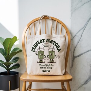 K&ouml;nnte beinhalten: Cremefarbene Tragetasche mit den Worten "Perfect Matcha" in einer Retro-Schriftart. Die Tasche zeigt eine Cartoon-Illustration von zwei Matcha-Getr&auml;nken mit Armen und Beinen. Der Text "What's Good in Hawaii" ist ebenfalls enthalten.