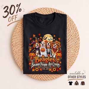 Peut inclure: Un t-shirt noir avec une illustration de quatre chiens beagle portant des costumes d'Halloween, dont une sorcière, un fantôme, un squelette et un épouvantail. Le texte indique Beagles, Because People Are Creepy, entouré de citrouilles et de feuilles.