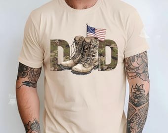May include: A beige t-shirt featuring the word "DAD" in a camouflage pattern. The "D" is filled with a green and brown camouflage design. The "A" and "D" have a pair of combat boots and an American flag.