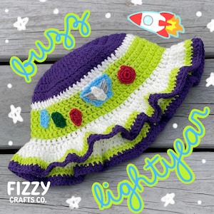 May include: A handmade crochet hat in the style of Buzz Lightyear, featuring purple, green, and white stripes. The hat has a ruffled brim and decorative appliques. The words "Buzz Lightyear" are written in a playful font.