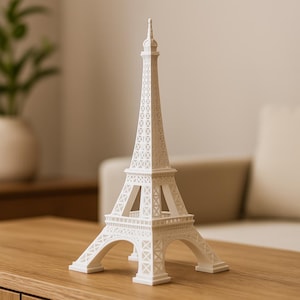 Puede incluir: Una réplica blanca de la Torre Eiffel, que muestra intrincados detalles de celosías y arcos. El monumento en miniatura se encuentra sobre una superficie de madera, capturando la esencia de la arquitectura parisina. Una pieza decorativa para el hogar o la oficina.
