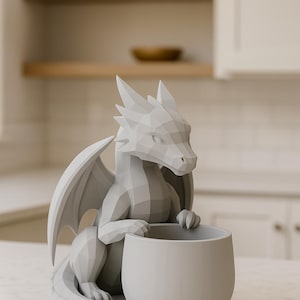 May include: A gray dragon-shaped planter with a geometric design. The dragon has wings and is holding a round planter. The planter is sitting on a white marble surface. The background is a blurred kitchen setting.