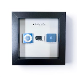 May include: A framed display featuring three blue iPod Shuffle components. The frame includes the text "iPod shuffle" and "8th generation, 2010". The components include a control pad, circuit board, and a clip.