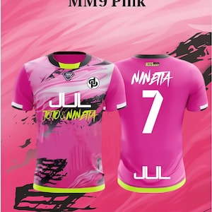 Op de afbeelding: Roze voetbalshirt met witte en zwarte accenten. De voorkant heeft de tekst "JUL TOTO & NINETA" en een logo. De achterkant toont de naam "NINETA" en het nummer "7". Het shirt heeft een zwarte kraag en witte mouwen.