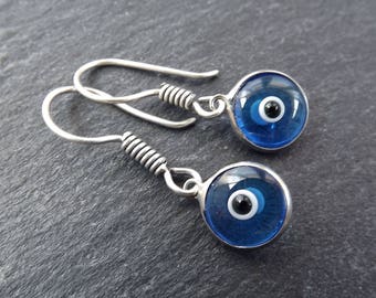 May include: A pair of silver earrings with blue evil eye charms. The charms are round and have a white center with a black pupil.