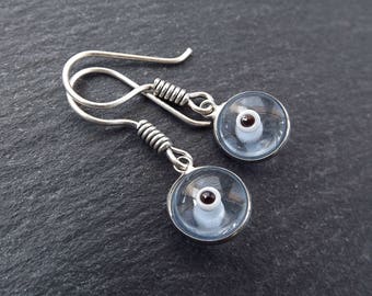 May include: Silver earrings with a clear glass cup design featuring a brown coffee bean inside.