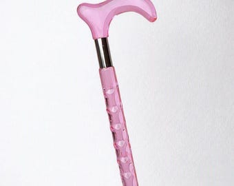 May include: A translucent pink walking cane featuring a smooth, curved handle and a textured, faceted shaft. A polished silver-colored metal collar connects the handle to the main body of the cane, providing a distinct contrast to the pink material.