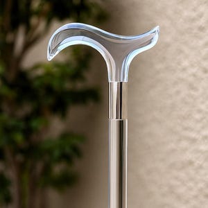 Puede incluir: Bastón de paseo de acrílico transparente con un mango curvo. El mango tiene una forma curva y transparente, y el eje es de color plateado pulido. El bastón está diseñado para soporte y movilidad.
