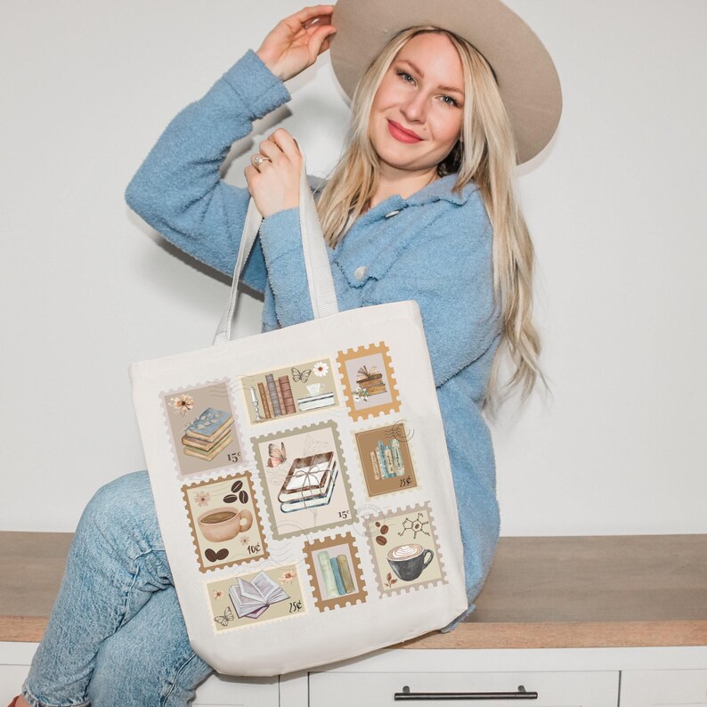 K&ouml;nnte beinhalten: Cremefarbene Tragetasche mit Briefmarkenmotiven mit Illustrationen von B&uuml;chern, Kaffeetassen und floralen Akzenten. Die Tasche hat eine rechteckige Form mit einem wei&szlig;en Griff und ist aus einem robusten Stoff gefertigt.