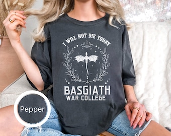 Könnte beinhalten: Dunkelgraues T-Shirt mit dem Text "I WILL NOT DIE TODAY" über einer Drachengrafik und den Worten "BASGIATH WAR COLLEGE". Das Shirt hat eine lockere Passform und kurze Ärmel. Die Farbe heißt "Pepper".