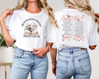 Könnte beinhalten: Weißes T-Shirt mit dem Text "READ BANNED BOOKS" und "KNOWLEDGE IS REBELLION" über einem offenen Buch mit floralen Akzenten. Auf der Rückseite des Shirts sind verbotene Bücher mit floralen Akzenten aufgeführt.