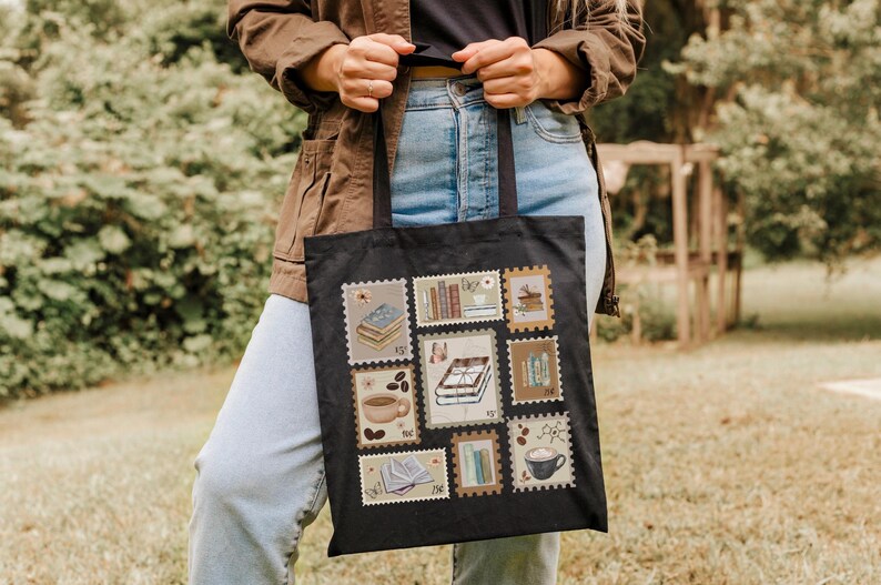 K&ouml;nnte beinhalten: Schwarze Tragetasche mit einer Collage von Briefmarken-Designs. Die Briefmarken zeigen B&uuml;cher, Kaffeetassen und andere literarische und Kaffee-bezogene Bilder. Die Tasche wird von einer Person gehalten, die eine braune Jacke und blaue Jeans tr&auml;gt.