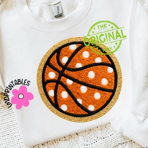 May include: White sweatshirt featuring a large basketball design. The basketball is orange with white polka dots, black lines, and a gold glitter border. The text "THE ORIGINAL" is stamped in green. The sweatshirt also has the text "UNDPRINTABLES" and a pink flower.