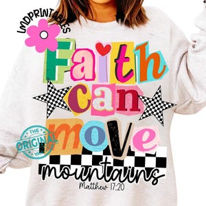 May include: A light gray sweatshirt with the words "Faith Can Move Mountains" in colorful, block letters. The design includes a heart, stars, and the Bible verse Matthew 17:20.