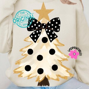 May include: Cream-colored sweatshirt featuring a Christmas tree design. The tree is gold with black polka dots and a black bow. A gold star tops the tree. The text "THE ORIGINAL" is printed on the upper left.