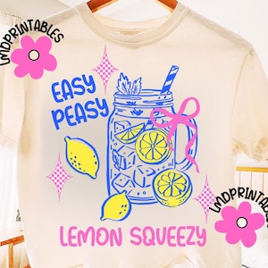 May include: A cream-coloured t-shirt featuring a blue and yellow lemonade design. The graphic shows a mason jar with ice, lemons, and a straw, along with the words "Easy Peasy Lemon Squeezy".