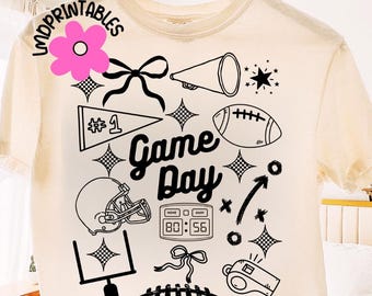 May include: Cream-colored t-shirt with a black graphic design featuring football-themed elements. The design includes a football, helmet, megaphone, and the words "Game Day". The shirt also has a score display and a whistle.