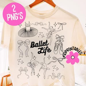 May include: Cream-colored t-shirt featuring a black line art design of ballet-themed elements. The design includes a tutu, ballet shoes, bows, dancers, and musical notes. The words "Ballet Life" are also printed on the shirt.