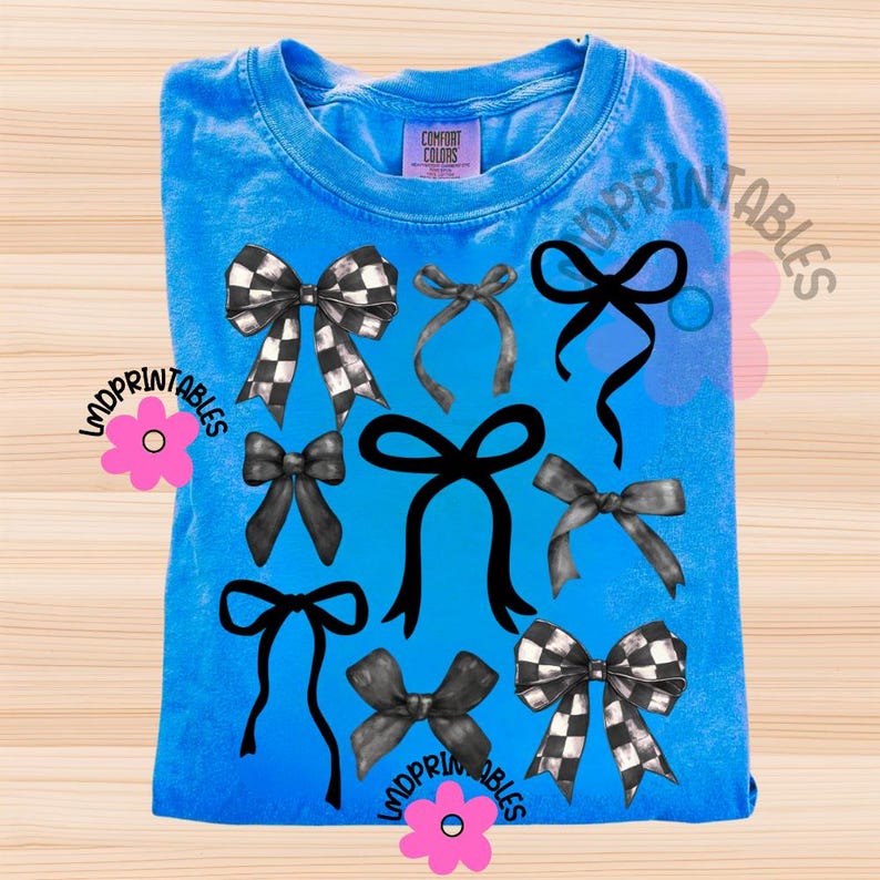 May include: A blue Comfort Colors t-shirt featuring a collection of black and white checkered and solid black bows. The bows are arranged in a pattern across the front of the shirt. The shirt has a crew neck and short sleeves.