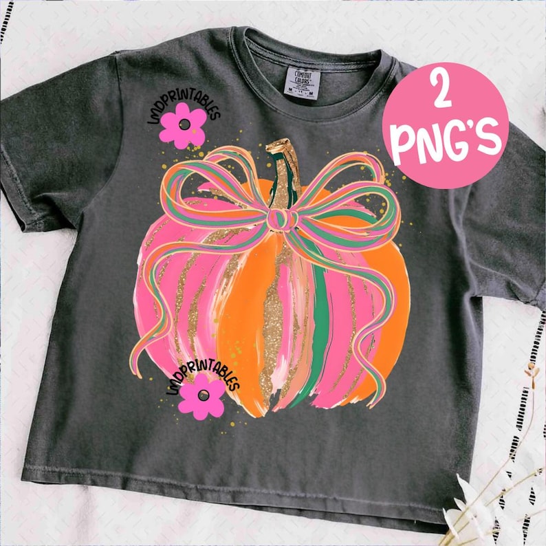 Peut inclure: T-shirt gris fonc&eacute; avec un motif de citrouille color&eacute;e. La citrouille est orange et rose avec un grand n&oelig;ud et des d&eacute;tails dor&eacute;s. Le t-shirt porte les inscriptions "WOOPPRINTABLES" et "2 PNG'S".
