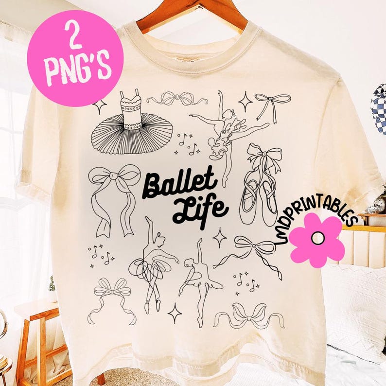 May include: Cream-colored t-shirt featuring a black line art design of ballet-themed elements. The design includes a tutu, ballet shoes, bows, dancers, and musical notes. The words "Ballet Life" are also printed on the shirt.