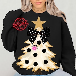 May include: Black sweatshirt featuring a Christmas tree design. The tree is beige with black polka dots and a black and white polka dot bow. A gold star tops the tree. The text "THE ORIGINAL 100%" is printed on the upper left.