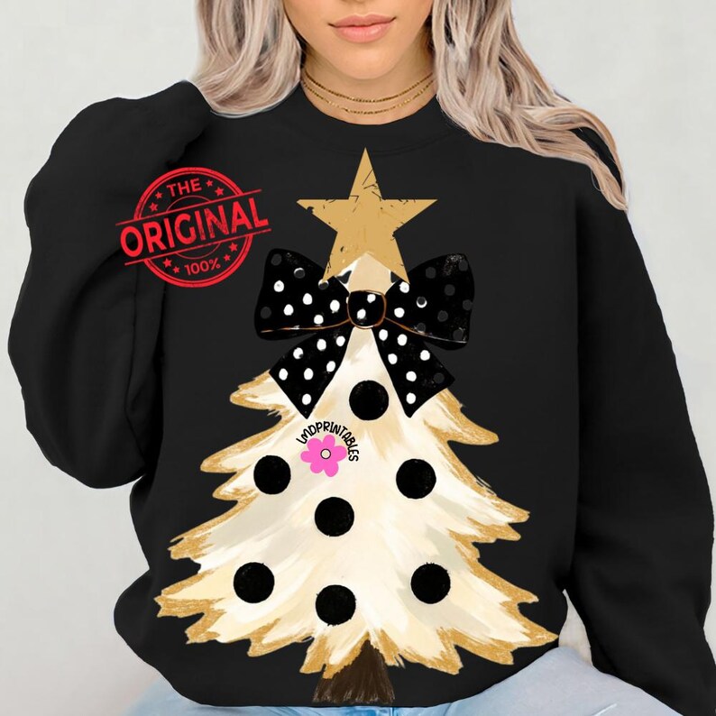 May include: Black sweatshirt featuring a Christmas tree design. The tree is beige with black polka dots and a black and white polka dot bow. A gold star tops the tree. The text "THE ORIGINAL 100%" is printed on the upper left.