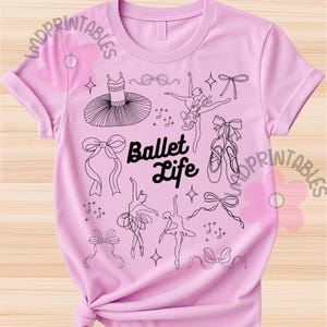 May include: A light pink t-shirt featuring a black and white illustration of ballet-themed elements. The design includes a tutu, ballet shoes, bows, dancers, and the words "Ballet Life".