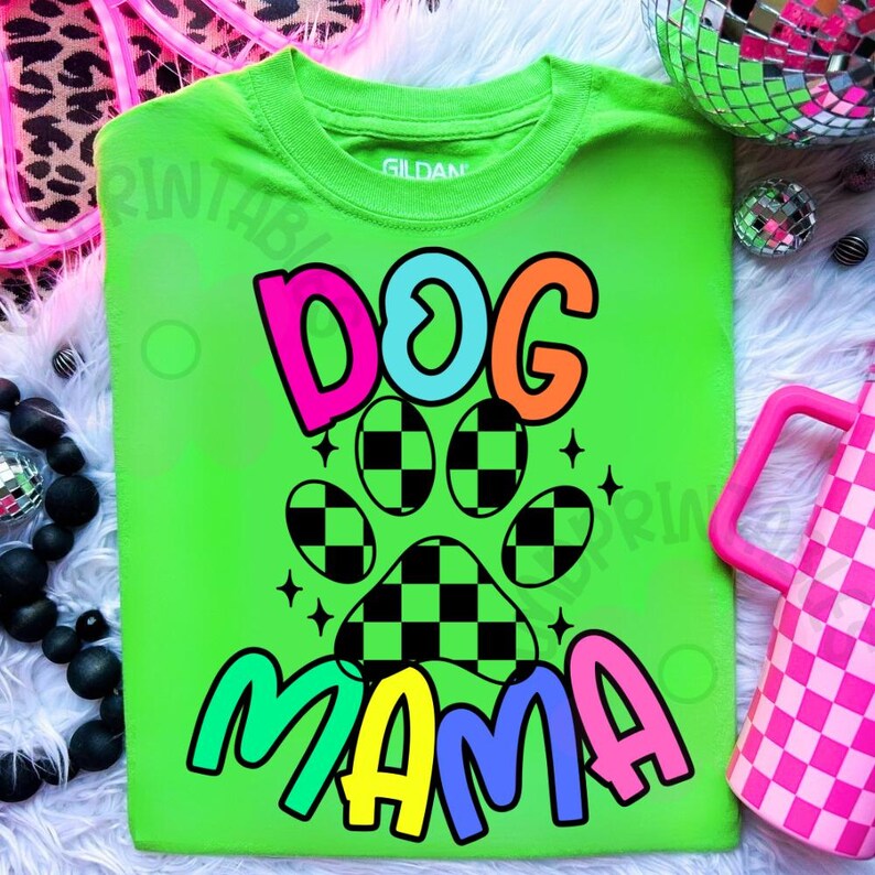 May include: A neon green t-shirt with the words "DOG MAMA" in a colorful, playful font. The design includes a paw print with a checkered pattern. The shirt is a Gildan brand.