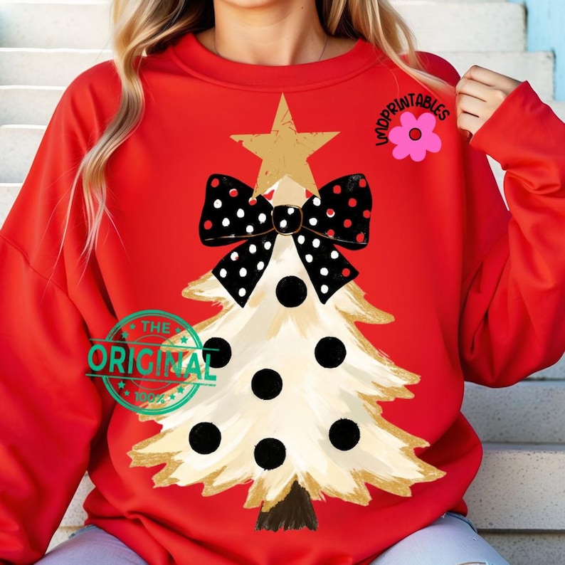 May include: A red sweatshirt featuring a Christmas tree design. The tree is beige with black polka dots and a gold star. A black bow with white polka dots sits above the tree. The text "THE ORIGINAL" is printed on the bottom left.
