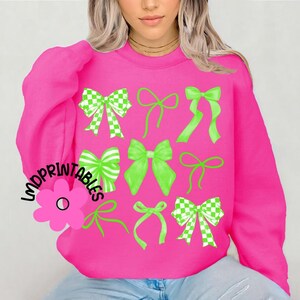 May include: A bright pink sweatshirt featuring a collection of green bows in various styles. Some bows have a checkered pattern, while others are solid green. The text "LMDPRINTABLES" is printed on the left side of the sweatshirt.
