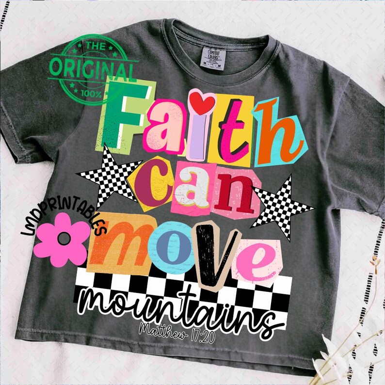 May include: Dark gray t-shirt with a colorful graphic design. The design features the words "Faith Can Move Mountains" in various bright colors and fonts, along with a pink flower, checkered stars, and the text "Matthew 17:20".