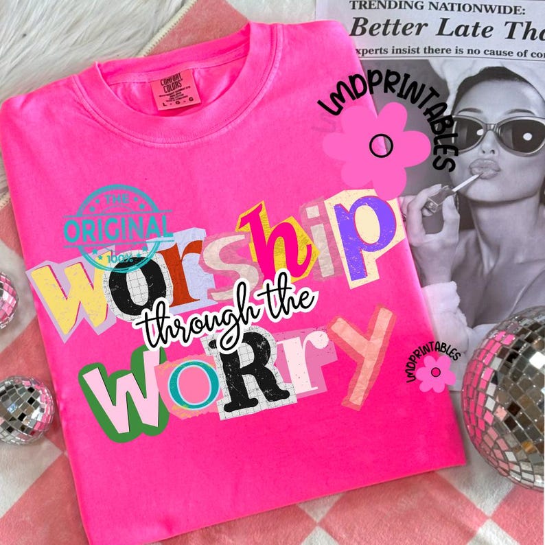 May include: A bright pink Comfort Colors sweatshirt with the words "Worship through the Worry" in a collage-style design. The text is in various colors and fonts. The shirt has a crew neck and long sleeves.