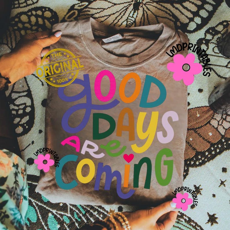 Może przedstawiać: Beżowa koszulka z napisem "GOOD DAYS ARE COMING" w kolorowych, zabawnych literach. Litery są w kolorach r&oacute;żowym, pomarańczowym, niebieskim, zielonym i ż&oacute;łtym. Koszulka ma okrągły dekolt i kr&oacute;tkie rękawy.