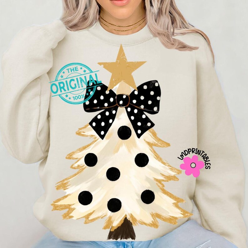 May include: Cream-colored sweatshirt featuring a Christmas tree design. The tree is gold with black polka dots and a black bow. A gold star tops the tree. The text "THE ORIGINAL" is printed on the upper left.