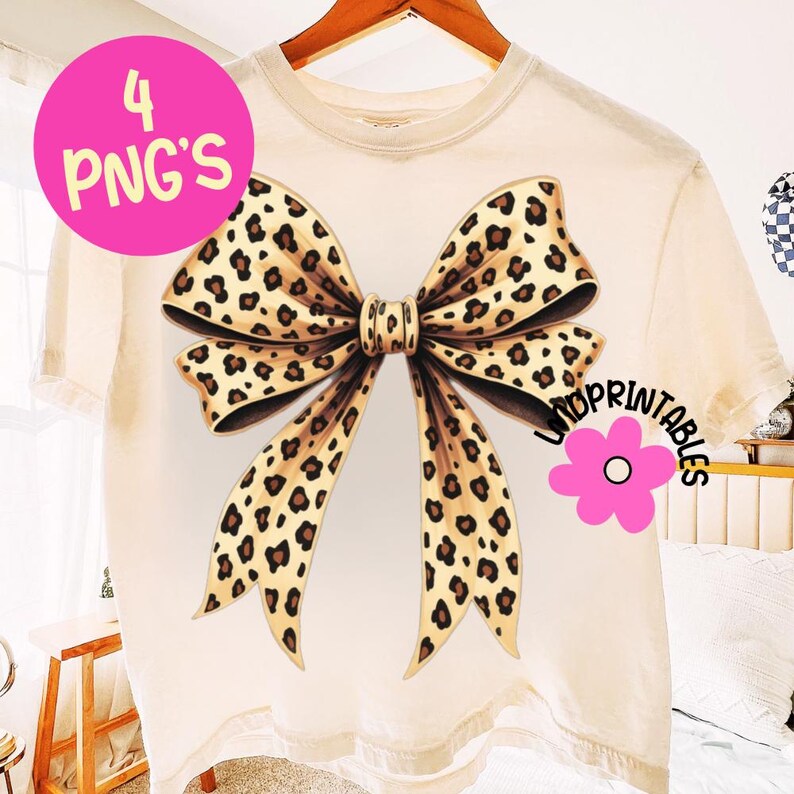 May include: Cream-colored t-shirt featuring a large bow design with a leopard print pattern. The bow is centered on the shirt and has a detailed, realistic appearance. The image also includes the text "4 PNG'S" in a pink circle and a pink flower with the text "JMDPRINTABLES".