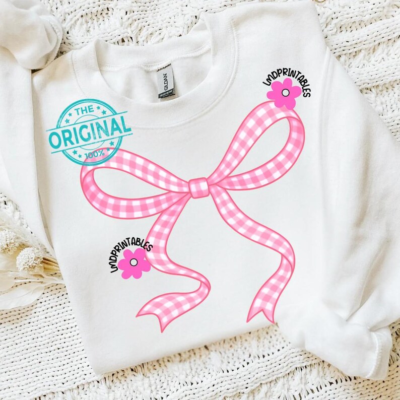May include: White sweatshirt featuring a large pink gingham bow design. The bow is accented with pink flowers and the text "LMDPRINTABLES". The text "THE ORIGINAL 100%" is printed on the upper left side of the sweatshirt.
