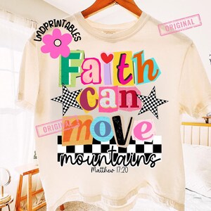 May include: Cream-colored t-shirt with a colorful graphic design. The design features the words "Faith can move mountains" in various bright colors and fonts, with checkered stars and the Bible verse Matthew 17:20.