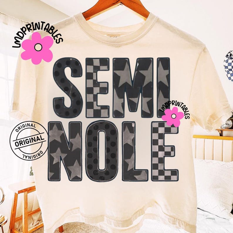 May include: Cream-colored t-shirt with the word "SEMINOLE" in large, bold letters. The letters have a mix of patterns, including stars, polka dots, and a checkered design. The shirt is hanging on a wooden hanger.