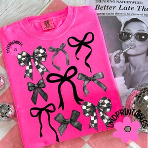 May include: Bright pink Comfort Colors sweatshirt featuring a collection of black and gray bows. Some bows have a checkered pattern. The text "LMDPRINTABLES" is visible on the design. A flower graphic is also present.