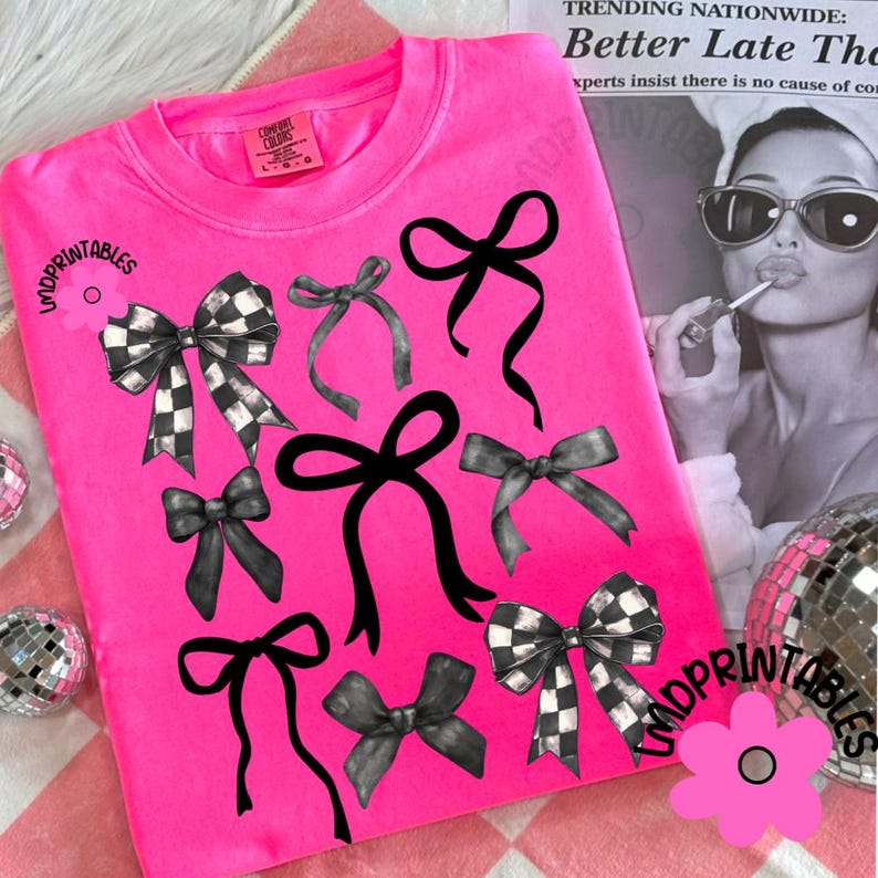 May include: Bright pink Comfort Colors sweatshirt featuring a collection of black and gray bows. Some bows have a checkered pattern. The text "LMDPRINTABLES" is visible on the design. A flower graphic is also present.