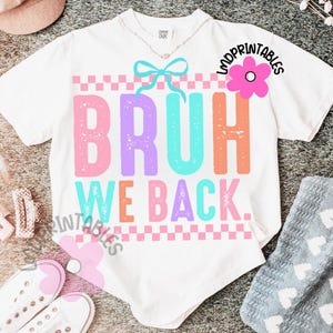 Puede incluir: Camiseta blanca con las palabras "BRUH WE BACK" en rosa, morado, naranja y turquesa. El dise&ntilde;o incluye un patr&oacute;n de cuadros y un lazo. La camiseta tiene un corte holgado.