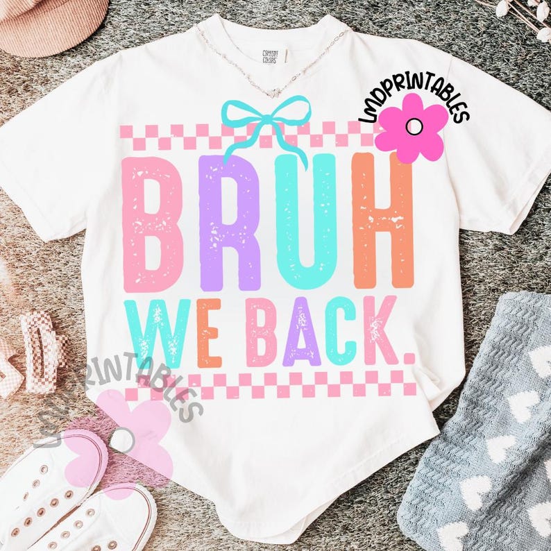 Puede incluir: Camiseta blanca con las palabras "BRUH WE BACK" en rosa, morado, naranja y turquesa. El dise&ntilde;o incluye un patr&oacute;n de cuadros y un lazo. La camiseta tiene un corte holgado.