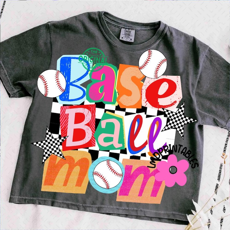 以下が含まれることがあります： 「Base Ball Mom」と書かれたカラフルなグラフィックが特徴の濃いグレーのTシャツ。デザインには野球ボール、星、花が含まれています。文字はさまざまな色とフォントで、チェック柄の背景になっています。