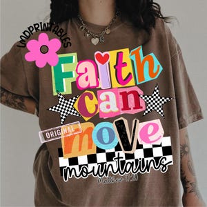 May include: Brown t-shirt with the words "Faith Can Move Mountains" in colorful, layered text. The design includes a heart, stars, and a checkered pattern. The text "Matthew 17:20" is also included.